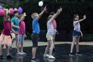 Zdjęcie przedstawia grupę dzieci tańczących na świeżym powietrzu. Za nimi zawieszone są balony.