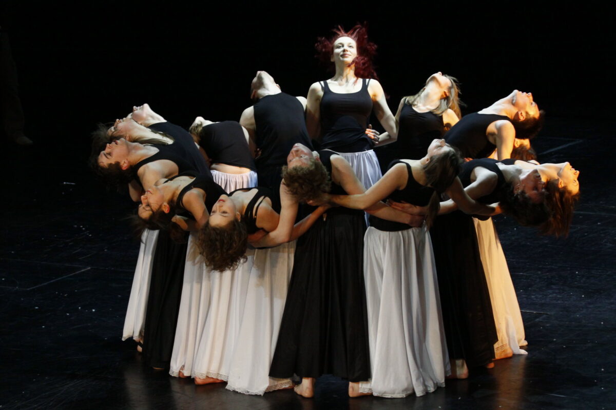 Grupa młodych tancerze na scenie, stoją ciasno spleceni w okręgu, głowy odchylone do tyłu