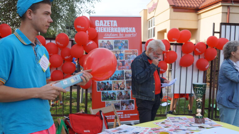 Stoisko promocyjne "Gazety Siekierkowskiej", na stole leżą egzemplarze gazety, stoisko jest udekorowane balonami i zdjęciami.