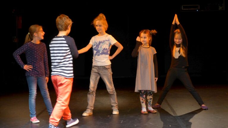 Zdjęcie przedstawia pięcioro dzieci na scenie. Wyglądają jakby odgrywali jakąś scenkę. Wśród dzieci są dwaj chłopcy i trzy dziewczynki.