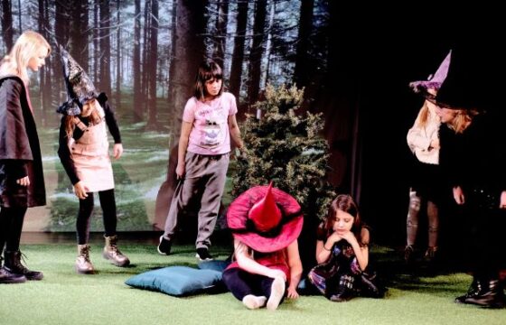 Kilka dziewczynek w kostiumach czarownic na scenie, za nimi las