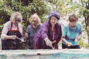 Cztery starsze kobiety pochylają się nad obrazem, który malują