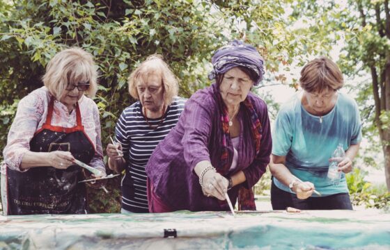 Cztery starsze kobiety pochylają się nad obrazem, który malują