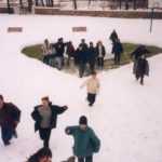 Zima. Grupa młodych ludzi, kilkoro biegnie po śniegu, kilkanaście osób stoi w miejscu odgarniętego śniegu w kształcie serca.
