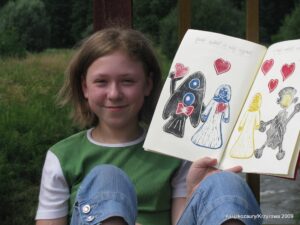 Dziewczynka z włosami do ramion pokazuje otwarty brulilon z rysunkami.