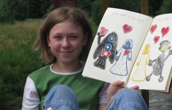 Dziewczynka z włosami do ramion pokazuje otwarty brulilon z rysunkami.