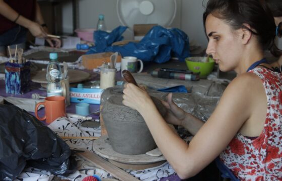 Pracownia plastyczna. Kobieta pracuje przy naczyniu najprawdopodobniej glinianym.