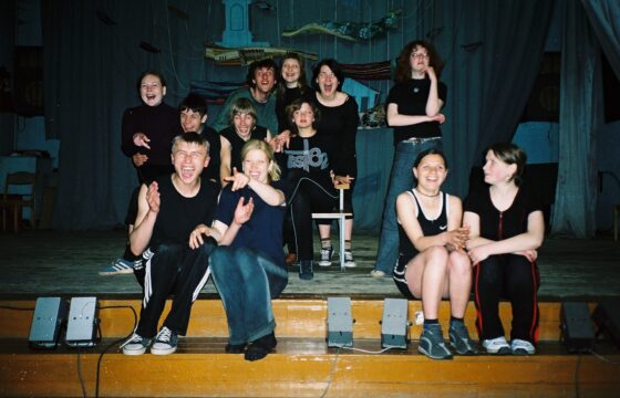 Zdjęcie grupowe chłopców i dziewcząt siedzących na scenie. Część z nich klaszcze, wszyscy są bardzo uśmiechnięci.