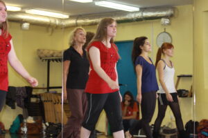 Zdjęcie przedstawia grupę 5 kobiet na sali tanecznej. Wszystkie idą w prawą stronę zdjęcia.