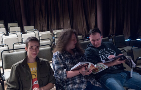 Zdjęcie przedstawia trzech młodych mężczyzn siedzących na widowni w teatrze.