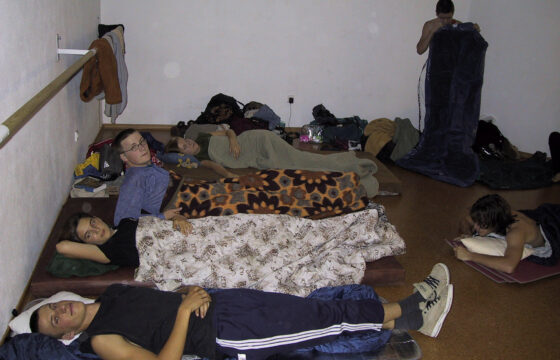 Zdjęcie przedstawia pięć osób leżących na podłodze w śpiworach i pod kocami.