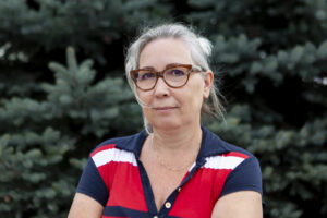 Zdjęcie przedstawia kobietę. Włosy ma zaczesana i upięte z tyłu. Ma okulary