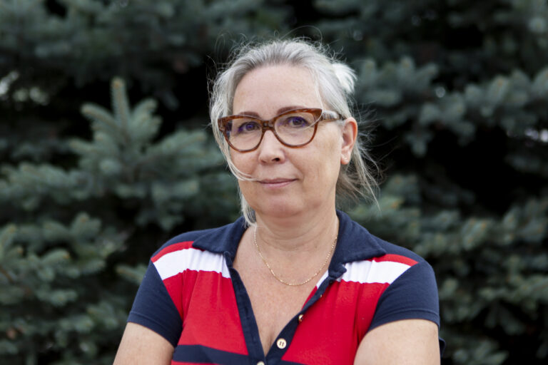 Zdjęcie przedstawia kobietę. Włosy ma zaczesana i upięte z tyłu. Ma okulary