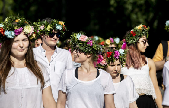 Grupa uśmiechniętych młodych ludzi, wszyscy mają na głowach wianki z żywych kwiatów.
