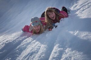 Zdjęcie, dwie dziewczynki leżą na brzuchach w śniegu