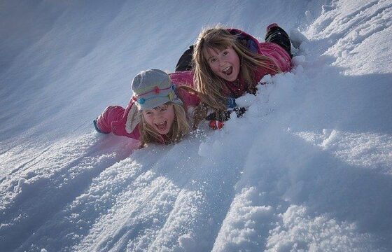 Zdjęcie, dwie dziewczynki leżą na brzuchach w śniegu