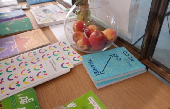 Zdjęcie przedstawia stół z publikacjami dotyczącymi tematu konferencji i wymiany polsko-niemieckiej. Na stole stoi również szklana misa w kształcie kuli z jabłkami w środku.