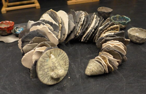 Zdjęcie przedstawia pracę ceramiczną w kształcie łańcucha składającego się z płaskich, okgrągłych elementów w kolorach ziemi.
