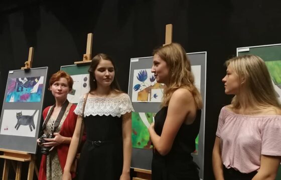 Zdjęcie przedstawia cztery kobiety stojące przed sztalugami z oprawionymi pracami graficznymi.