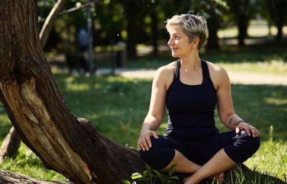 Kobieta w stroju do jogi siedzi po turecku w plenerze