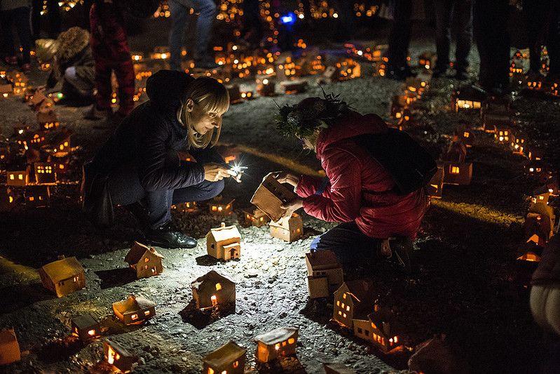 Miniaturowe gliniane domki. Jest ich bardzo dużo. Rozstawione są na ziemi na dużej przestrzeni, wewnątrz nich palą się malutkie świeczki. Pośród nich wędrują ludzie