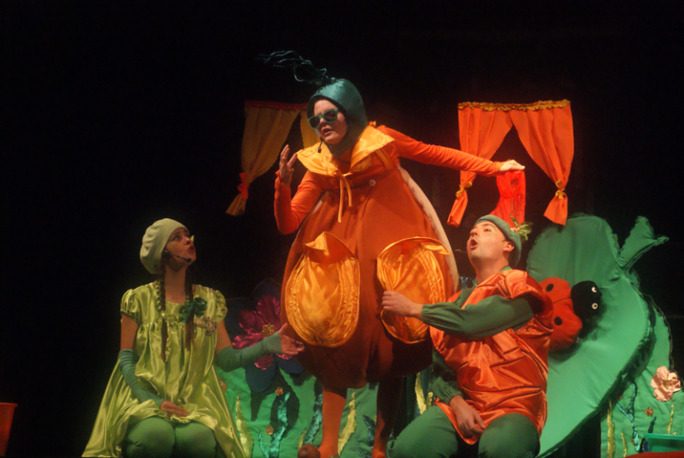 Zdjęcie przedstawia scenę z bajki dla dzieci - trzy postacie w kostiumach warzyw.