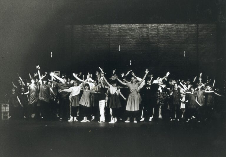 Duża grupa młodzieży na scenie, stoją w różnych pozach z rękami wyrzuconymi do góry