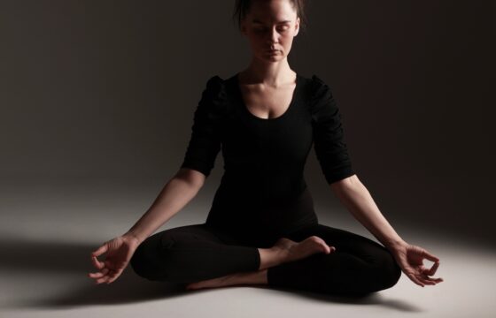 Młoda kobieta ćwicząca jogę, jest w pozycji siedzącej z rękoma opartymi o kolana, ma przymknięte oczy