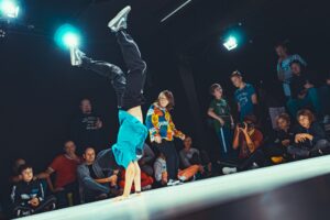 Chlopiec na scenie tańczy breakdance, stoi na rękach, za nim widownia