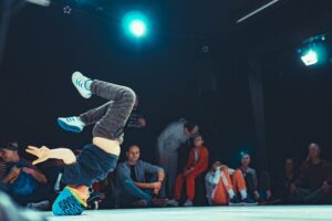 Chłopiec na scenie tańczy breakdance, stoi na głowie, za nim siedzi widownia