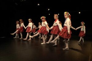 Grupa dzieci w wieku przedszkolnym na scenie w strojach ludowych - tańczą