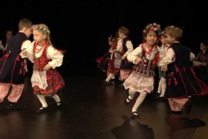 Grupa dzieci w wieku przedszkolnym na scenie w strojach ludowych- tańczą