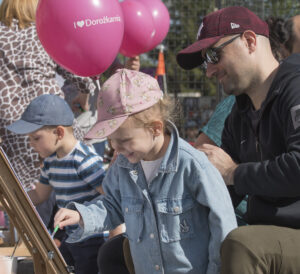 Dzieci malujące na sztalugach, nad nimi unoszą się dwa balony