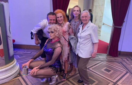 Grupa starszych kobiet i jeden mężczyzna pozują do zdjęcia w towarzystwie drag queen
