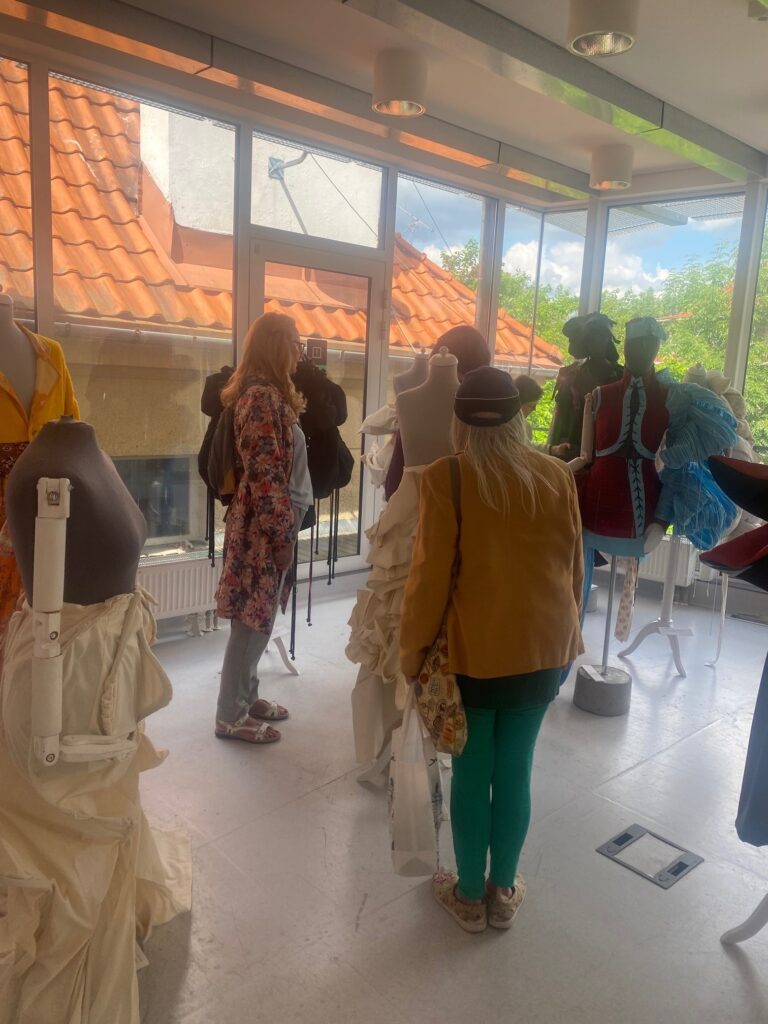 Grupa dojrzałych kobiet ogląda wystawę strojów kobiecych prezentowaną na manekinach