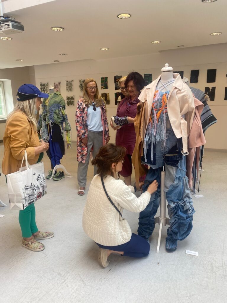Grupa dojrzałych kobiet ogląda wystawę mody kobiecej prezentowaną na manekinach.