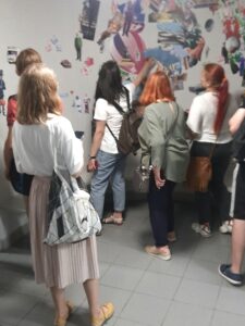 grupa 6 osób stojąca tyłem do obiektywu, patrzy na białą ścianę udekorowaną magnetycznymi obrazkami