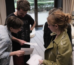 Trzy osoby stoją zwrócone do siebie i patrzą na kartki z instrukcjami, które trzymają w rękach.