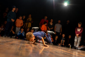 Kilkuletni chłopiec tańczy breakdance, wokół niego widownia