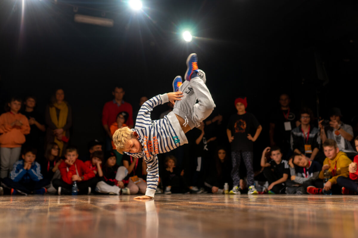 Chłopiec na scenie tańczący breakdance, wokół niego na podłodze siedzą widzowie