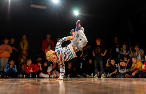 Chłopiec na scenie tańczący breakdance, wokół niego na podłodze siedzą widzowie
