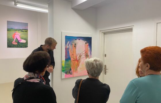 Trzy kobiety i mężczyzna patrzą na obrazy zawieszone na ścianie w galerii
