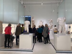 Grupa seniorek i seniorów ogląda rzeźby stojące na podestach w muzeum