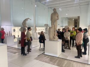 Grupa seniorek i seniorów ogląda eksponaty we muzeum, m. in. rzeźby stojące na podestach