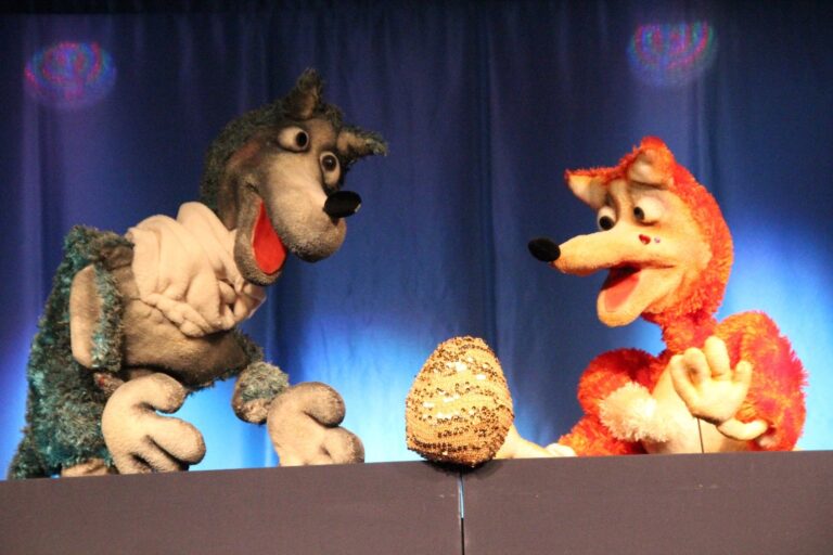 Dwie kukiełki, z lewej wilk, z prawej lis. Między nimi jest duże jajko