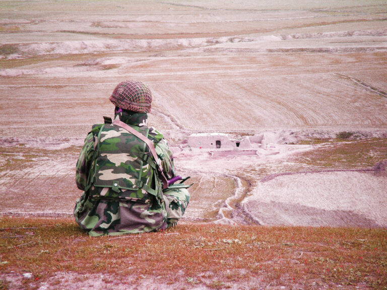 Żołnierz w umundurowaniu bojowym siedzi na poligonie