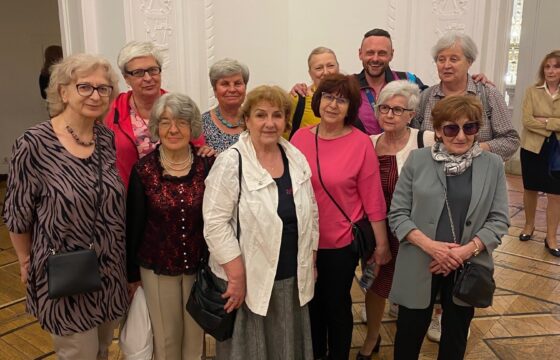 Grupa seniorek i młody mężczyzna pozują do zdjęcia w pomieszczeniu