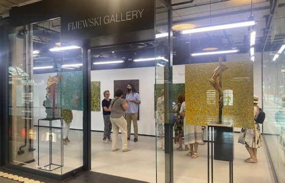 Kilka kobiet i mężczyzna w przeszklonym budynku wystawowym z napisem Fijewski Gallery.