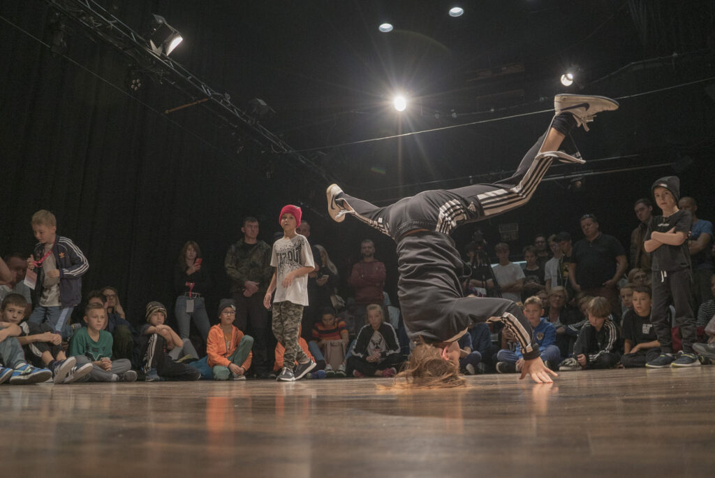 Chłopak tańczący breakdance - za nim na podłodze siedzi publiczność