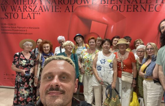 Grupa seniorek pozuje do zdjęcia, są elegancko ubrane. Na pierwszym planie młody mężczyzna